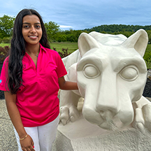PSU-LV的女学生穿着亮粉色的新生迎新领导衬衫微笑着, 站在PSU-LV狮子神殿旁边.