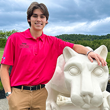 PSU-LV的男学生穿着亮粉色的新生迎新领导衬衫微笑着, 站在PSU-LV狮子神殿旁边.
