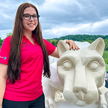 PSU-LV的女学生穿着亮粉色的新生迎新领导衬衫微笑着, 站在PSU-LV狮子神殿旁边.