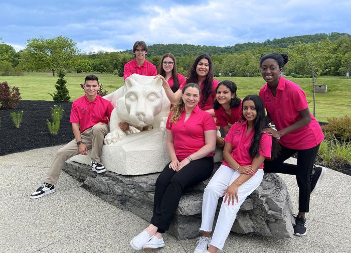 8名身穿粉色迎新衫的宾州州立大学学生聚集在宾州州立大学狮子神社雕像周围.