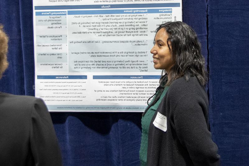Girl with dark curly hair wearing a black cardigan presents research poster