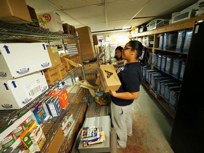 Young woman sorting donations and stacking boxes on shelf