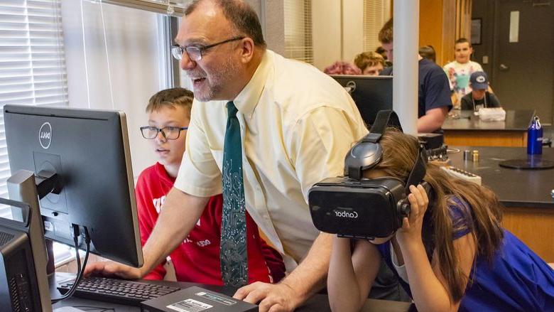 Michael Gallis assists middle schoolers who are trying on VR headsets.