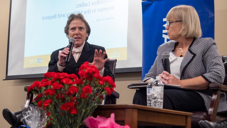 two women on a stage ; one speaking