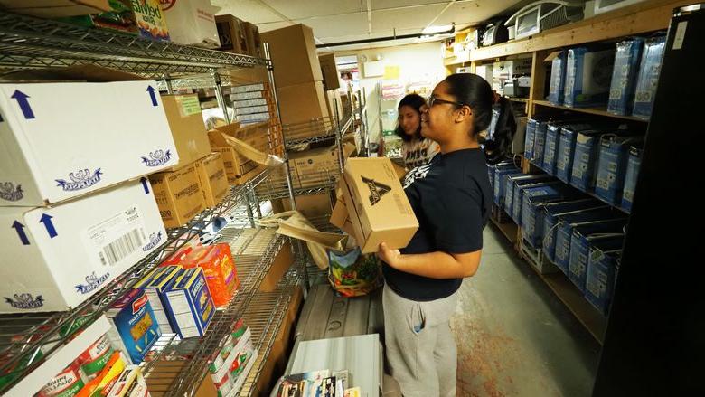 Young woman sorting donations and stacking boxes on shelf